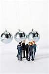 Group of businessmen figurines standing in circle, Newton's cradle in background