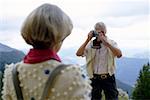 Senior adult man taking a picture of his wife in the mountains, selective focus