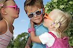 Two girls trying to kiss a boy, all wearing sunglasses, close-up