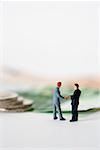 Two businessmen figurines shaking hands, money in background