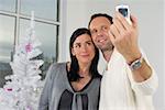 Couple photographing themselves with a mobile phone in front of a white Christmas tree