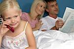 Little blond girl is phoning in front of the bed of her parents, selective focus