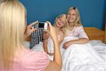 Blond woman taking a picture of her two daughters who are sitting in bed, close-up