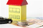Car, toy house and a stack of coins on Euro banknotes