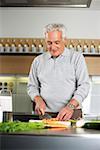 Gray-haired man is cutting vegetables in a kitchen, selective focus