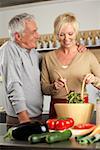 Gray-haired man watching a blonde woman making salad