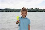 Little boy in front of a lake with a water pistol, close-up, selective focus