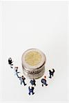 Group of businessmen figurines around a stack of coins