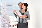 Couple holding a present next to a white Christmas tree