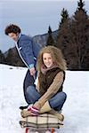 Young man pulling a sled with a blonde woman sitting on it