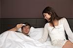Young brunette woman is sitting at the edge of a bed while her boyfriend is looking at a pregnancy test