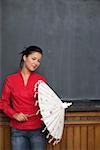 Asian woman is holding an umbrella in front of a blackboard