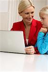 Blond girl is sitting next to her mother behind a laptop, close-up