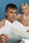 Father lying in bed with daughter and wife and is reading a financial paper, close-up