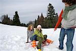 Young man pulling a sled with two women sitting on it