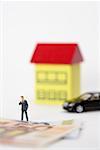 Businessman figurine between Euro banknotes, a house and a car