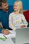 Man sitting behind a laptop with his daughter while drawing in a sketchbook