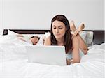 Woman Using Laptop Computer in Bed while Man Sleeps