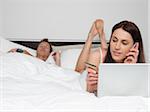 Woman Shopping Online while Man Watches TV in Bed