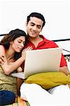 Young man using a laptop on the bed with a young woman leaning on him