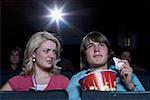 Boy with tissues crying at movie theater with girl watching