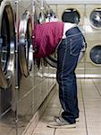 Side profile of man with head and arms in dryer at Laundromat