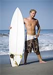 Portrait of a young man standing on the beach with a surfboard