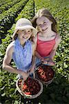 Portrait de deux jeunes filles avec des paniers de fraises sur un champ