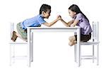 Boy and girl sitting at table arm wrestling