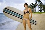 Porträt einer jungen Frau hält ein Surfbrett und stehen am Strand