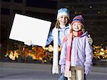 Two girls outdoors in winter with blank sign