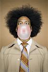 Man with an afro in beige suit blowing a bubble