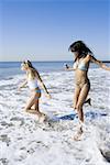 Profile of two young women running in the water on the beach