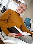 Low angle view of an elderly man reading a book and smiling