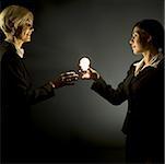 Younger businesswoman giving light bulb to mature businesswoman