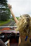 Rear view of a young woman sitting in a car with her hand raised