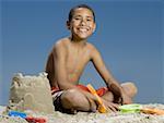 Portrait of a boy sitting beside a sand castle