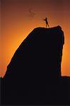 Silhouette d'une personne debout au sommet d'un rocher jeter une corde