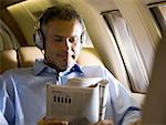 A businessman listening to music on headphones and reading a magazine in an airplane