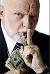 Portrait d'un homme d'affaires avec son doigt sur les lèvres et détenant des billets de cent dollars