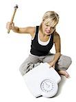 Frustrated dieting woman smashing bathroom scale with a hammer