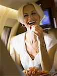 A businesswoman eating fruit and laughing in an airplane