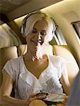 A businesswoman listening to music from an MP3 player in an airplane