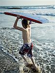 Boy running at the beach with a boogie board.