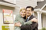 Portrait of a couple hugging in front of house with 'Sold' sign