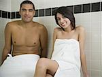 Man and woman in steam bath with towels smiling