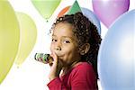 Young girl wearing party hat and playing amongst balloons