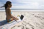 Profil einer jungen Frau, die mit einem Laptop am Strand