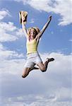 Low angle view of a young woman holding her hat and jumping