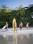 Mid adult couple and a young couple standing on the beach with surfboards